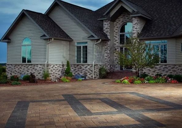 Large suburban house with stone façade, dark roof, and brick driveway in front