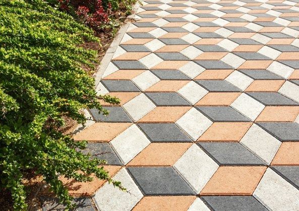 Geometric patterned walkway with tan, white, and gray pavers beside green shrubs