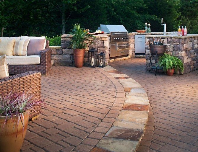Outdoor patio with wicker seating, stone pavers, potted plants, and a built-in grill at sunset