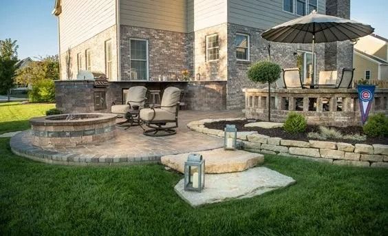 Patio with stone seating, umbrella table, and lantern beside a house and green lawn