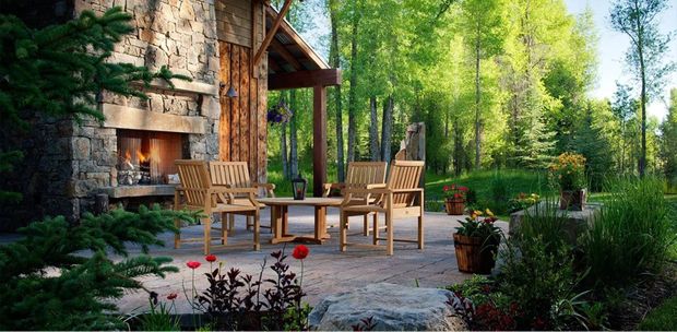 Rustic stone patio with wooden chairs and table amid lush green garden and trees