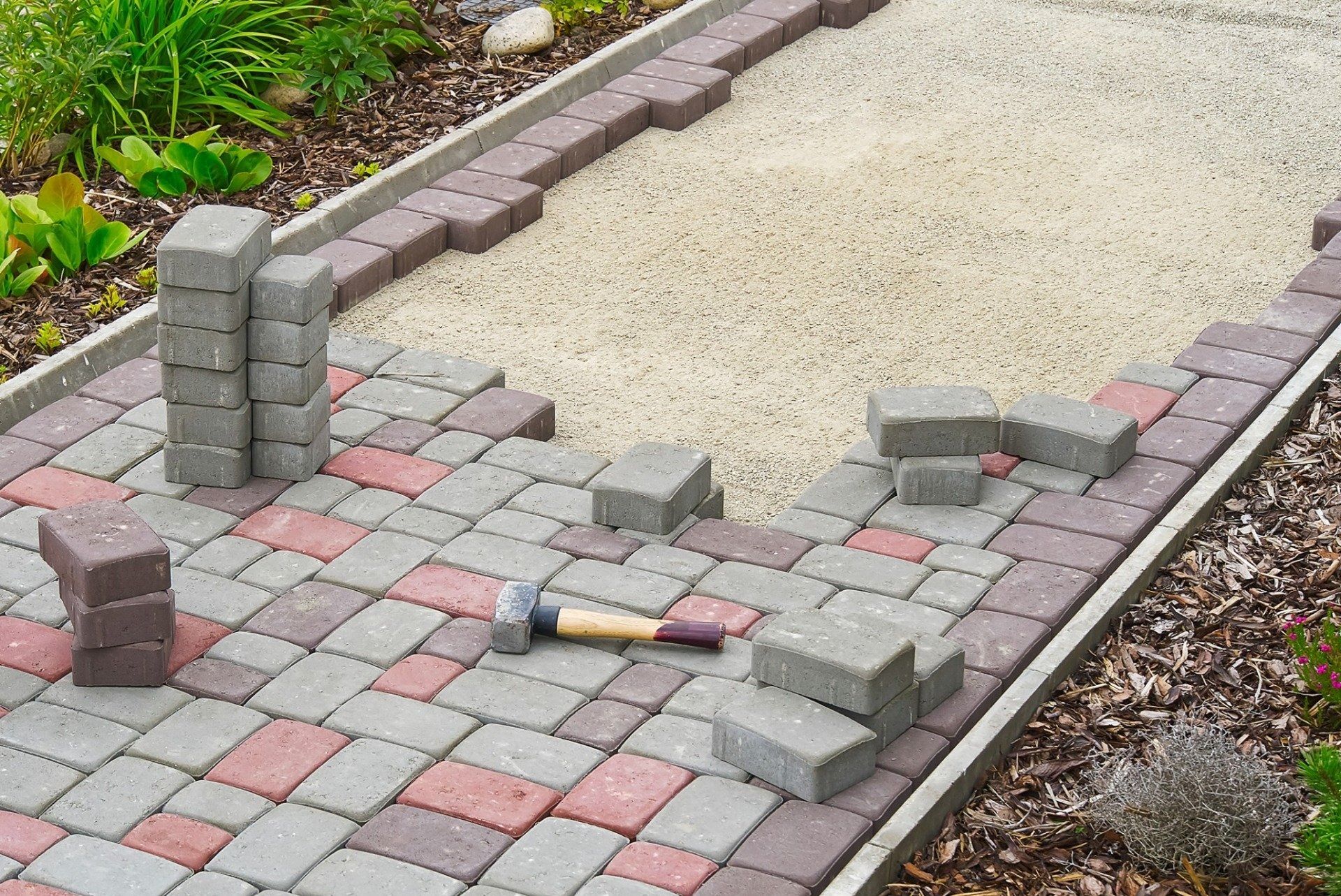 Broken paver walkway with loose bricks and a hammer beside the damaged section