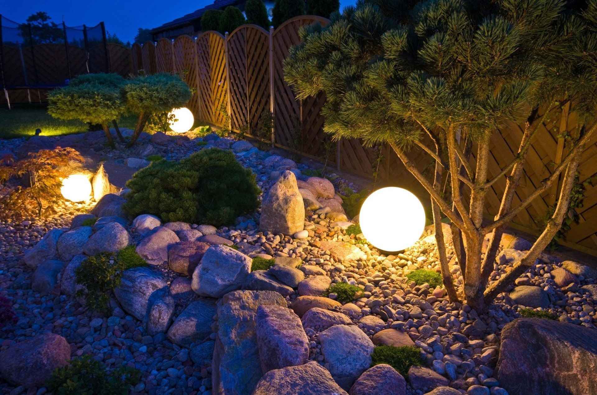 Illuminated rock garden at night with glowing spherical lights and trees along a stone path