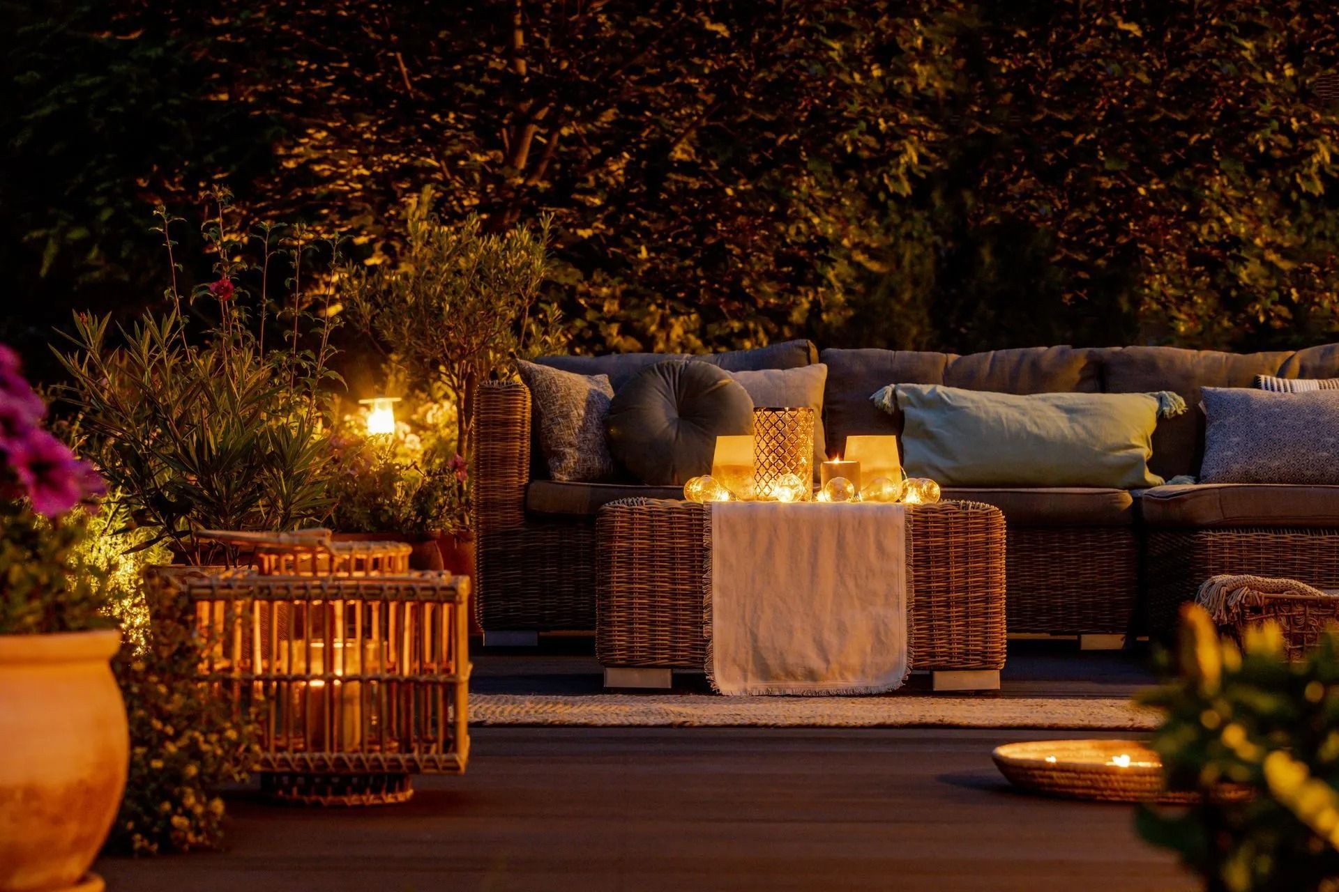 Cozy outdoor patio with wicker sofa, cushions, candles, and warm string lights at night