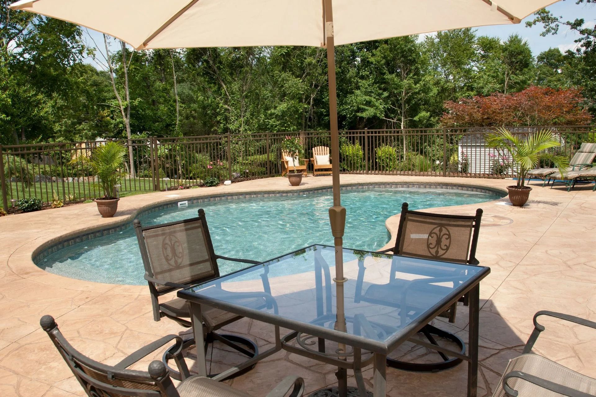 Backyard pool patio with glass table, chairs, and large umbrella by the pool