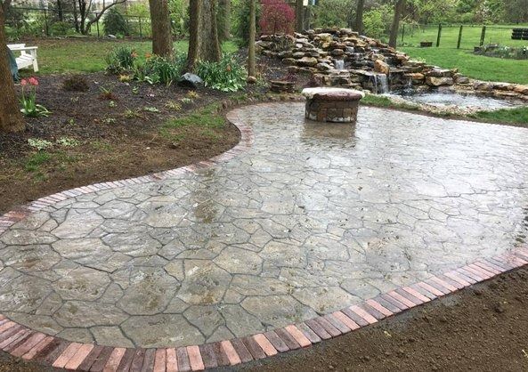 Curved stone patio with brick border and a central bench in a wooded garden setting