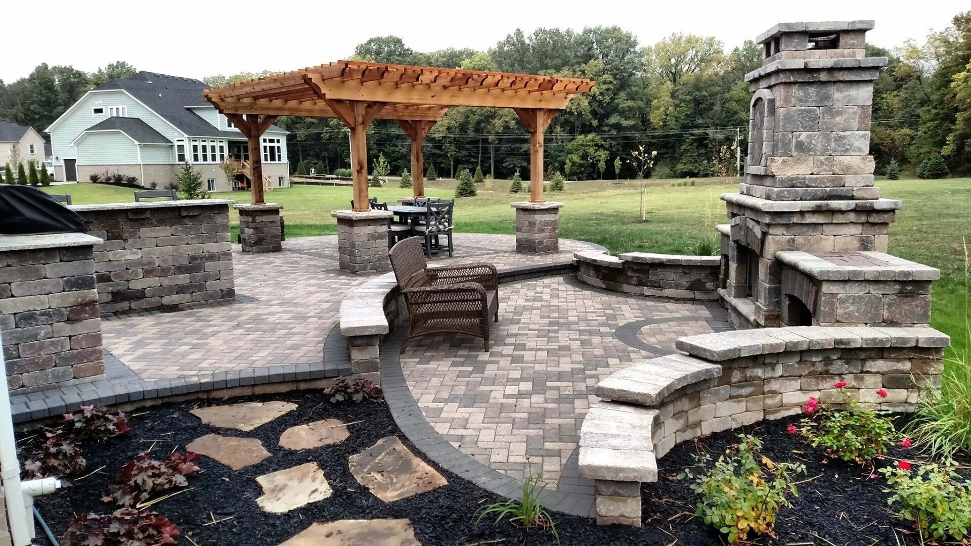 Backyard patio with stone fire pit, wooden pergola, brick seating, and landscaped flower beds