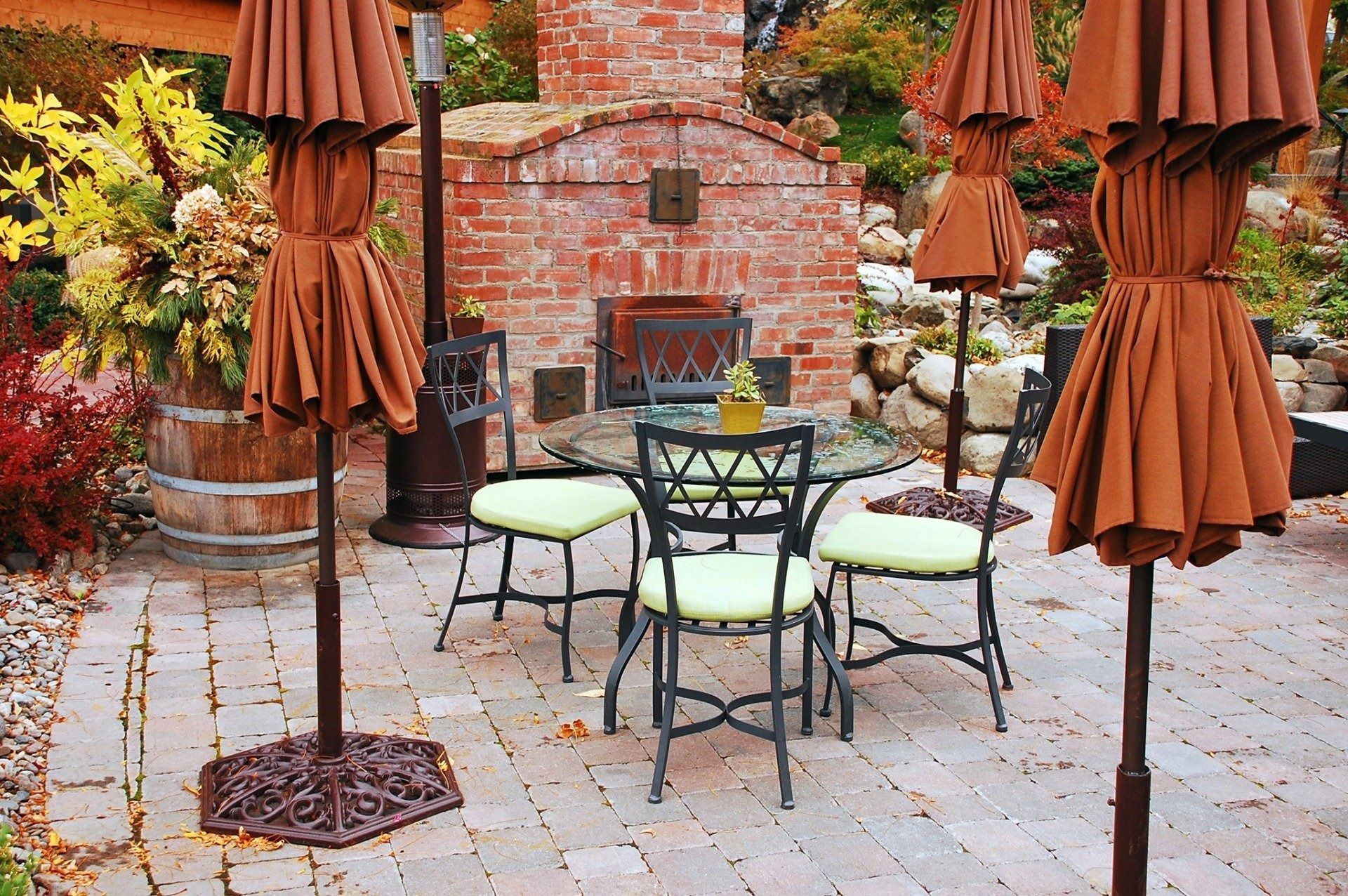 Empty outdoor patio with brown umbrellas, metal chairs, and a brick fireplace in autumn colors