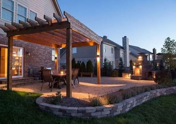 Backyard patio with wooden pergola, lit dining area, and modern house at dusk