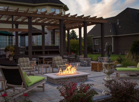 Backyard patio with pergola, wicker seating, and a lit fire pit at dusk