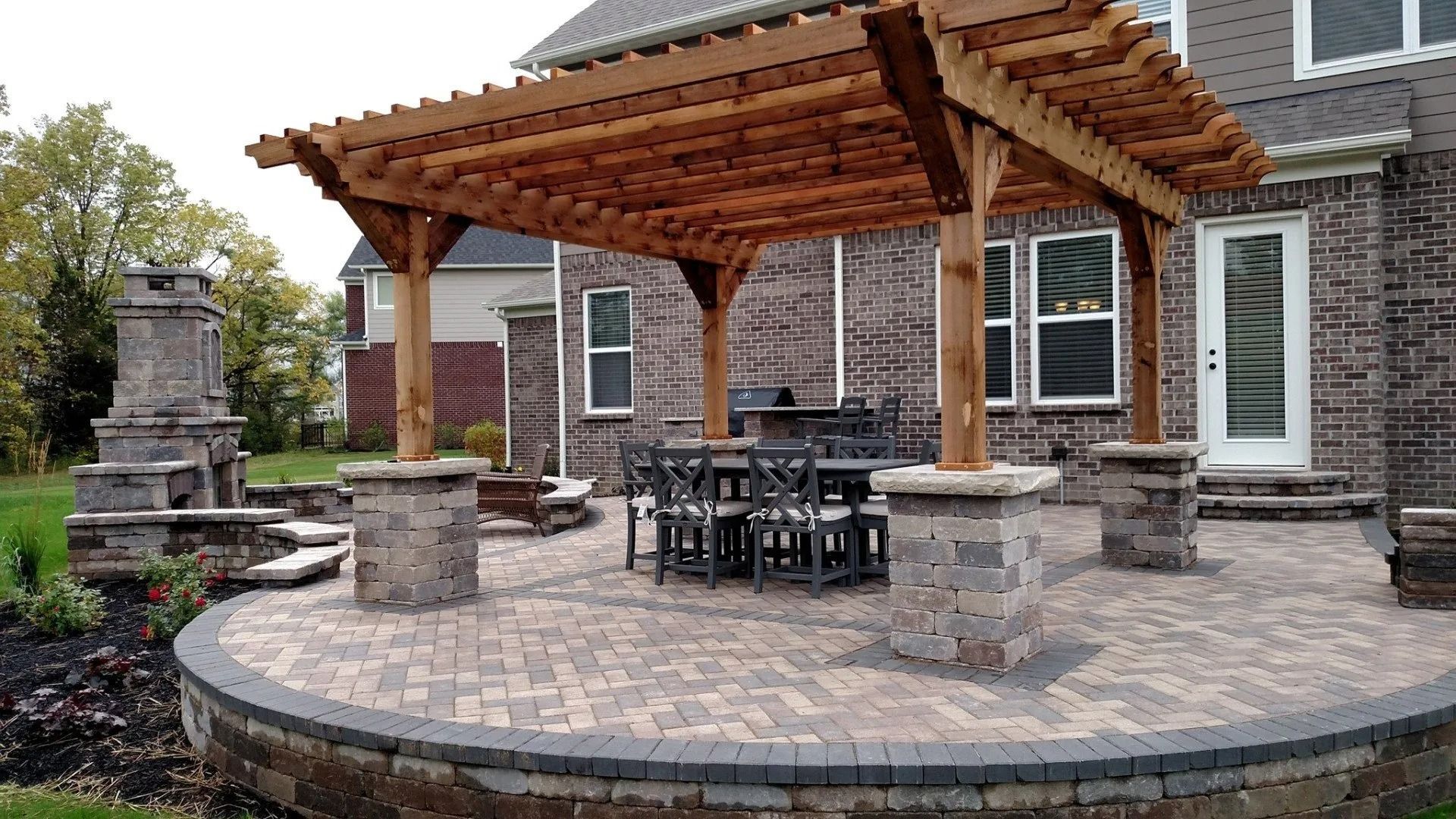 Stone patio with a wooden pergola, outdoor dining set, and brick house in the background