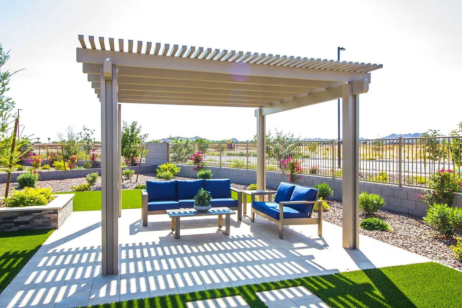Outdoor patio with a pergola, blue cushioned seating, and a small table on a landscaped lawn.