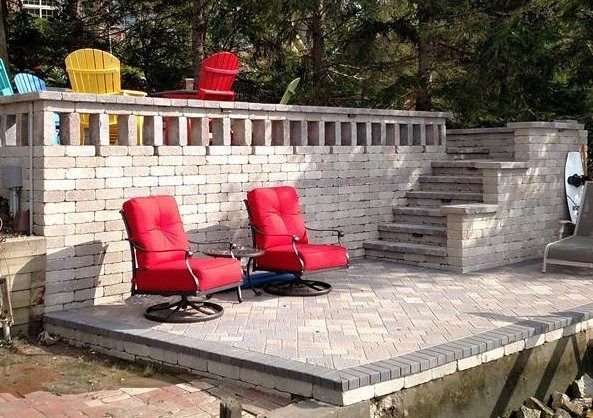 Outdoor patio with two red lounge chairs beside a white brick wall and steps leading to a raised deck.