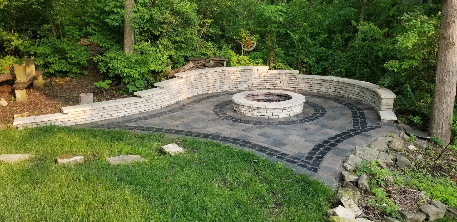 Curved stone fire pit with built-in bench seating in a green landscaped backyard
