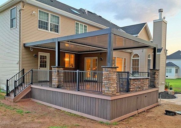 Two-story house with a covered backyard deck, stone pillars, and black railing at dusk