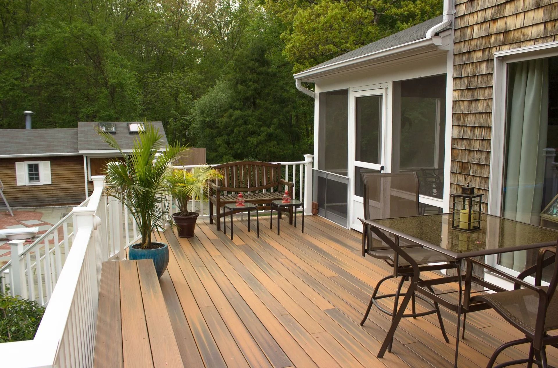 Wooden backyard deck with patio table, chairs, potted plants, and sliding glass doors on a house