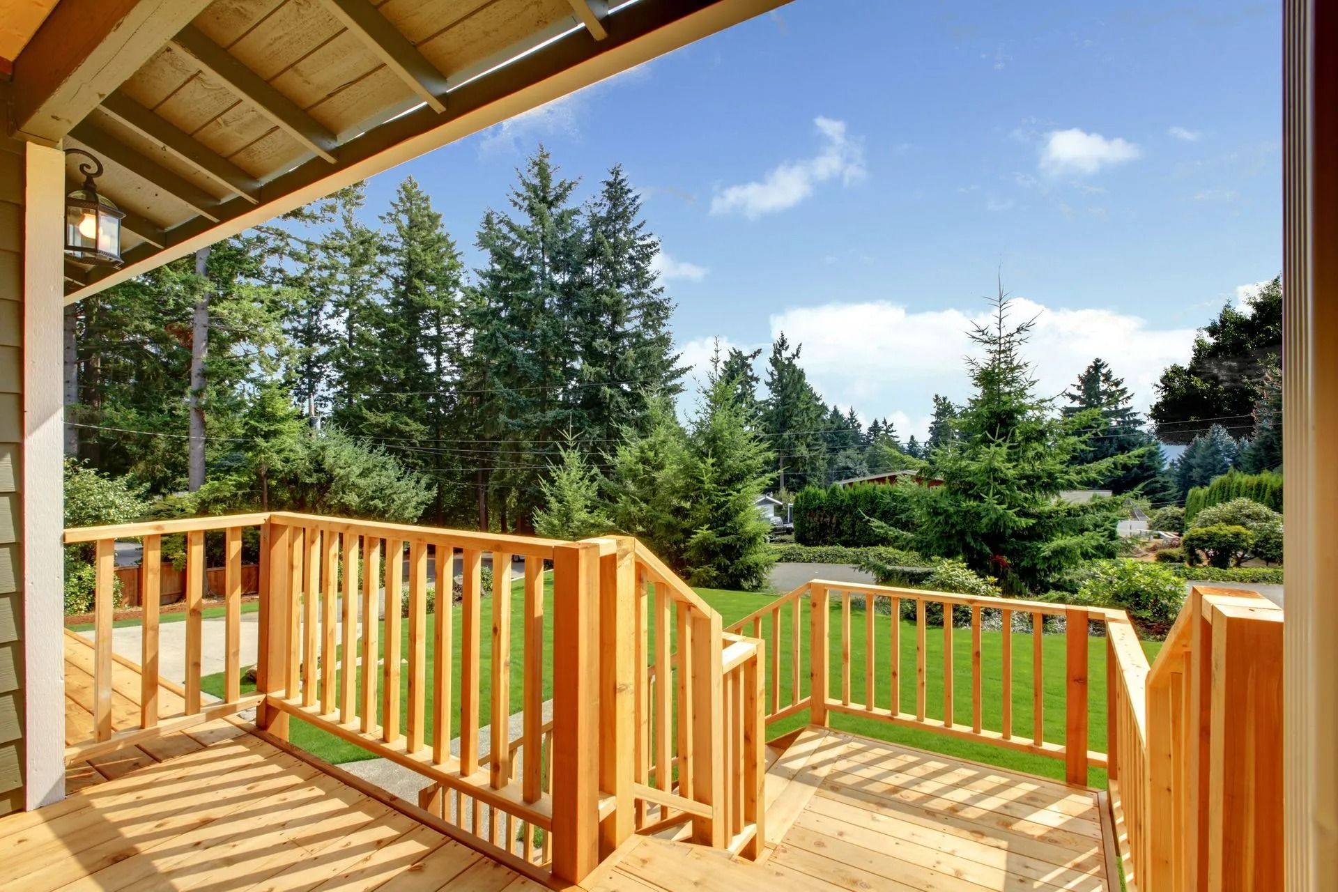 Wooden deck and railing overlooking a green backyard with trees under a blue sky.