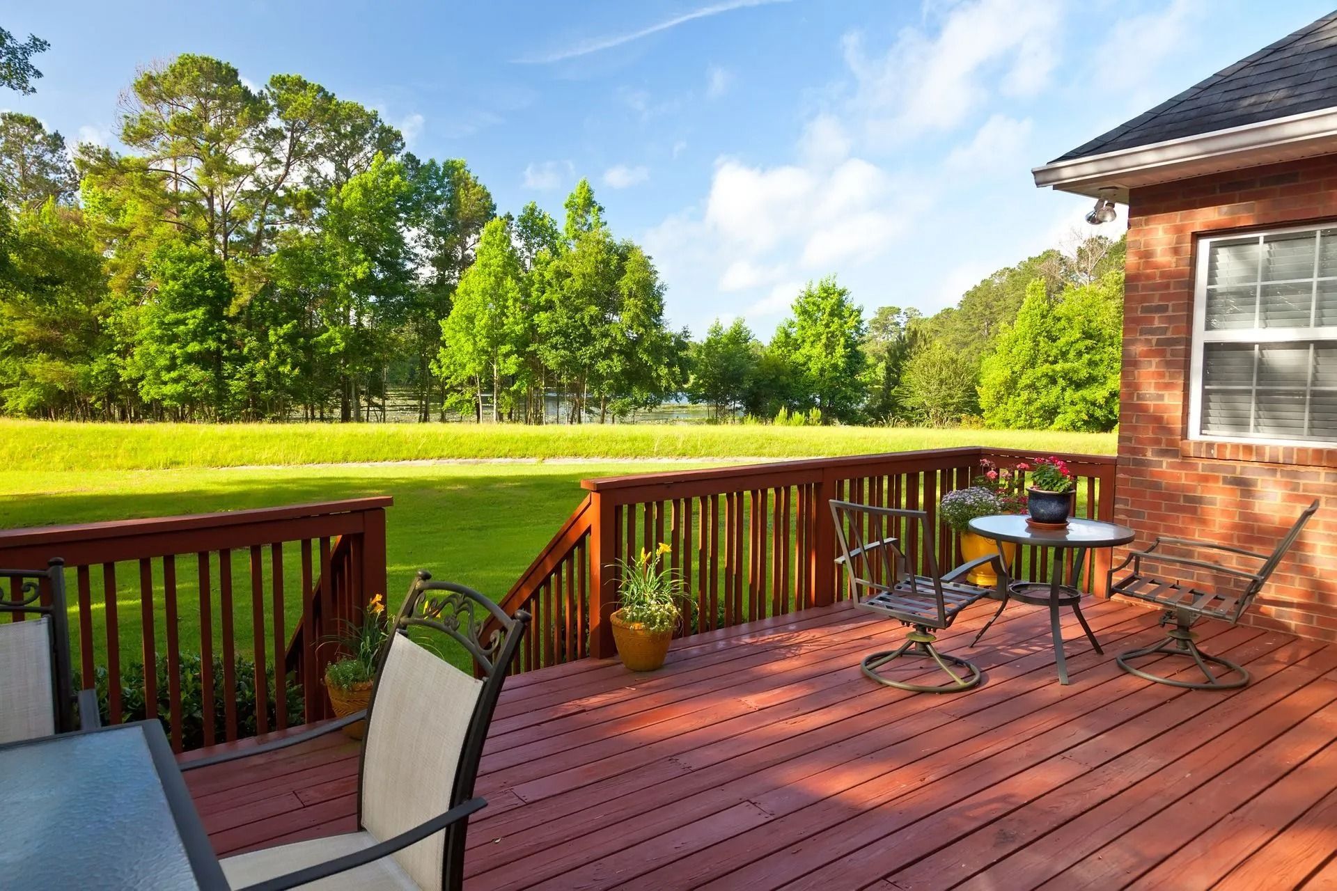 Wooden deck with chairs overlooking a green lawn and trees beside a brick house