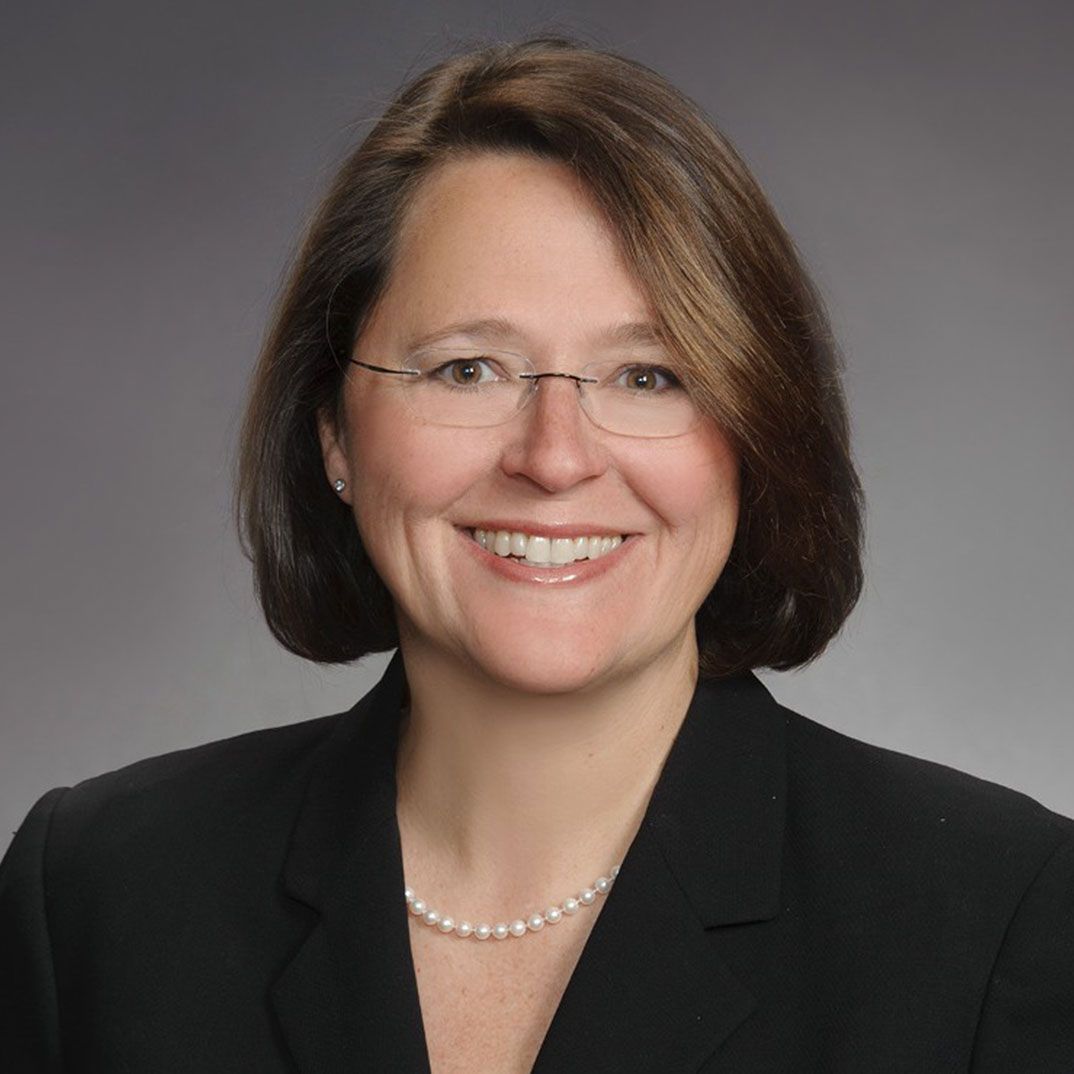 A woman wearing glasses and a pearl necklace smiles for the camera