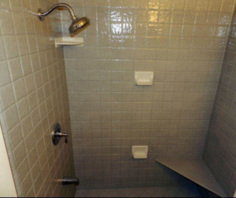 Gray-tiled shower with showerhead, fixtures, soap dishes, and a built-in seat.