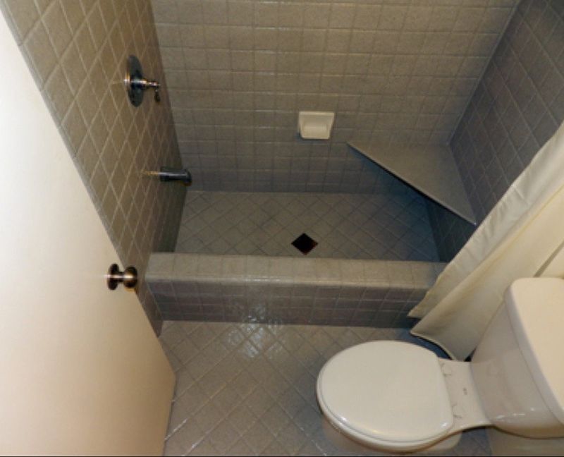 Gray tiled bathroom with shower and toilet, seen from above.