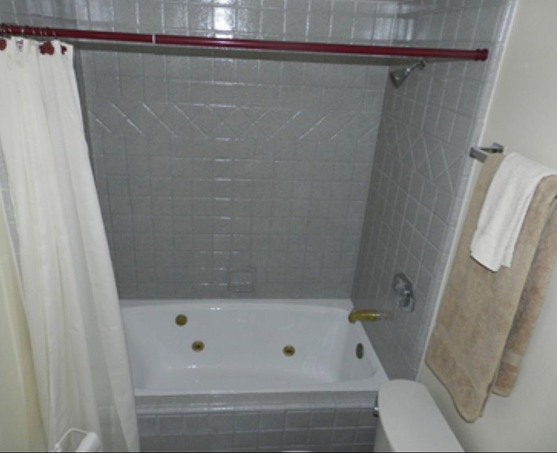 Bathroom with white tub, grey tile, white shower curtain, and a tan towel.