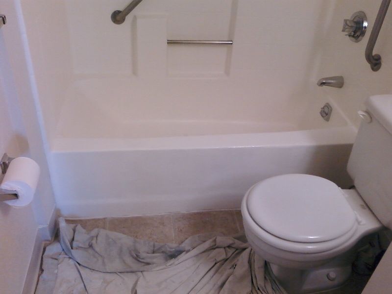 A white bathroom with a toilet and bathtub. A grab bar is above the tub.