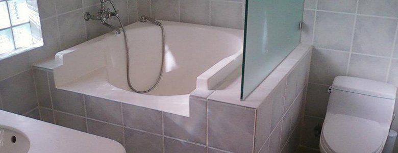 A bathroom with a built-in bathtub, glass shower partition, and toilet. Tile walls.