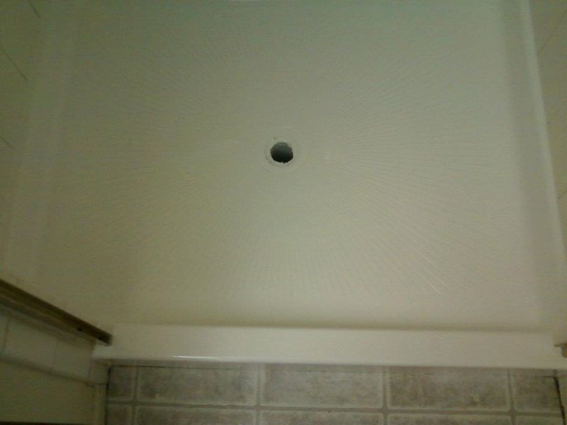 Hole in a white shower ceiling, above tiled wall and countertop.