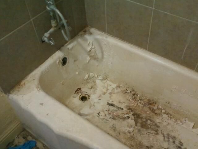 A dirty, damaged bathtub with peeling material, surrounded by beige tiles.