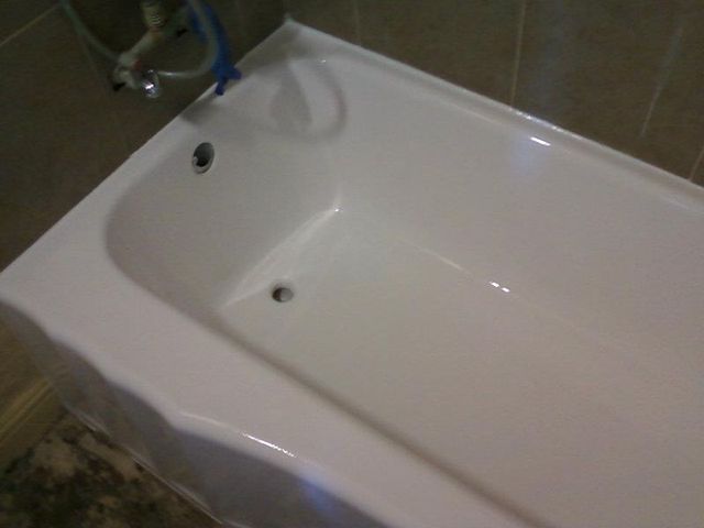 White bathtub in a tiled bathroom, faucet on the wall, two jets on the side.