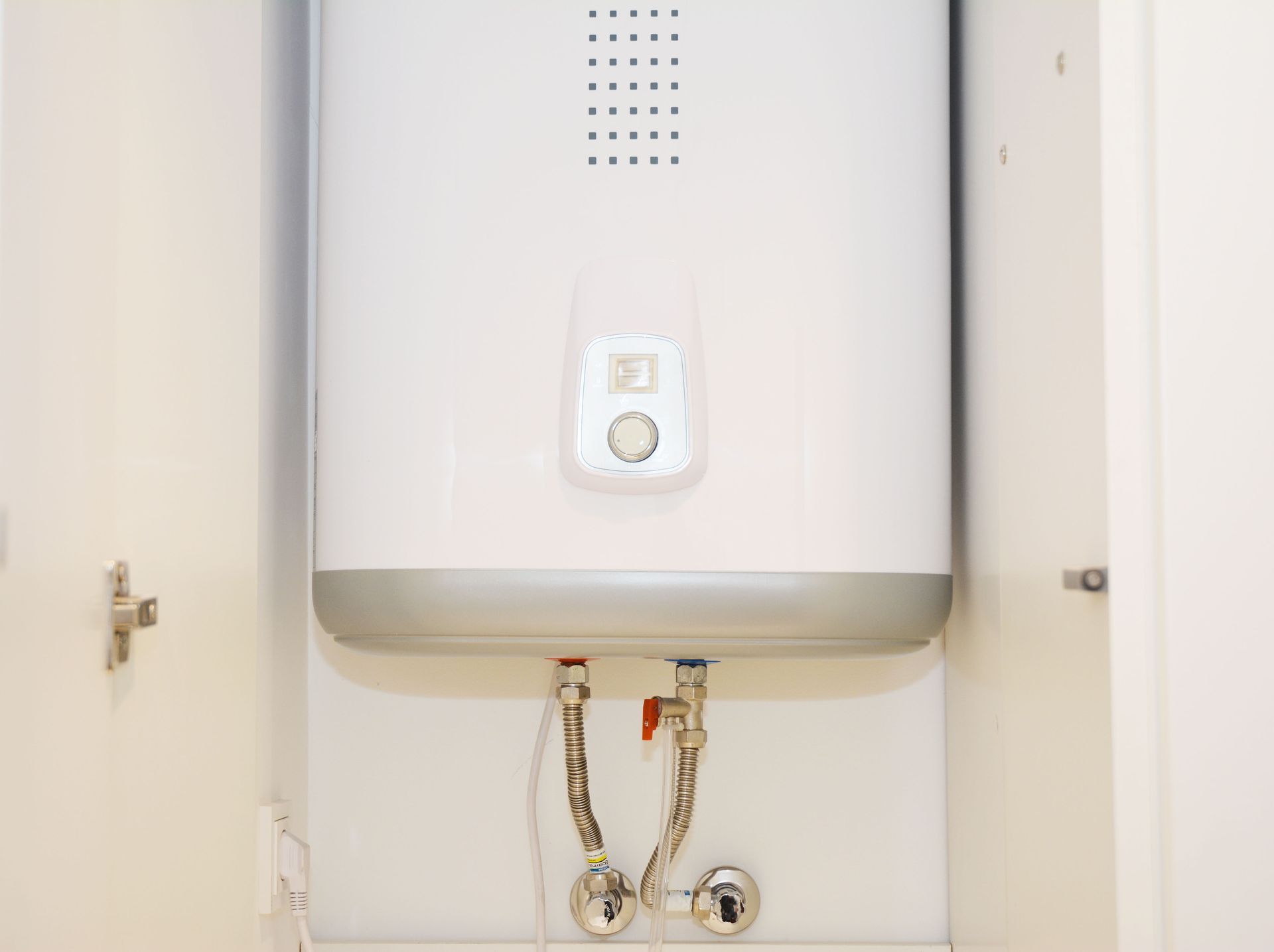 White wall-mounted water heater with exposed pipes in a cabinet opening