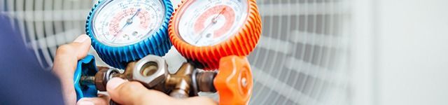Close-up of HVAC gauges and valves on an air conditioning unit with blue and orange dials