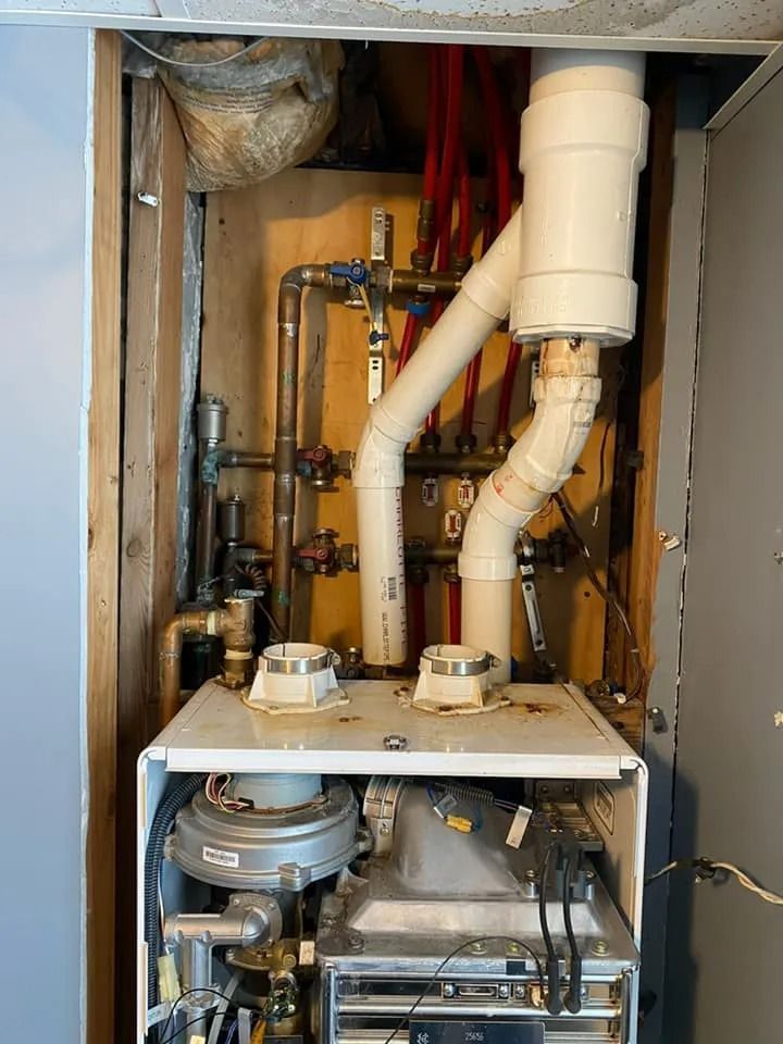 Open utility cabinet with pipes, valves, and white drainage tubing in a wall cavity
