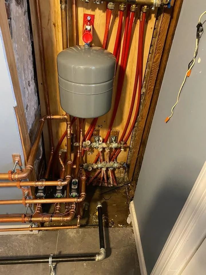 Plumbing pipes and a gray expansion tank in a utility room, with red PEX tubing and copper lines.