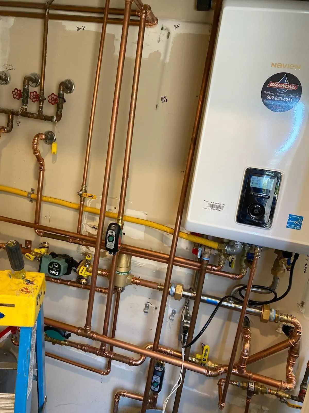 Wall-mounted boiler and copper pipes in a utility room, with a white water heater on the right.