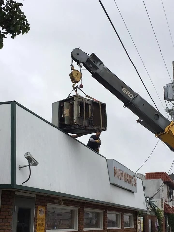 Crane lifting a large metal unit onto a building rooftop