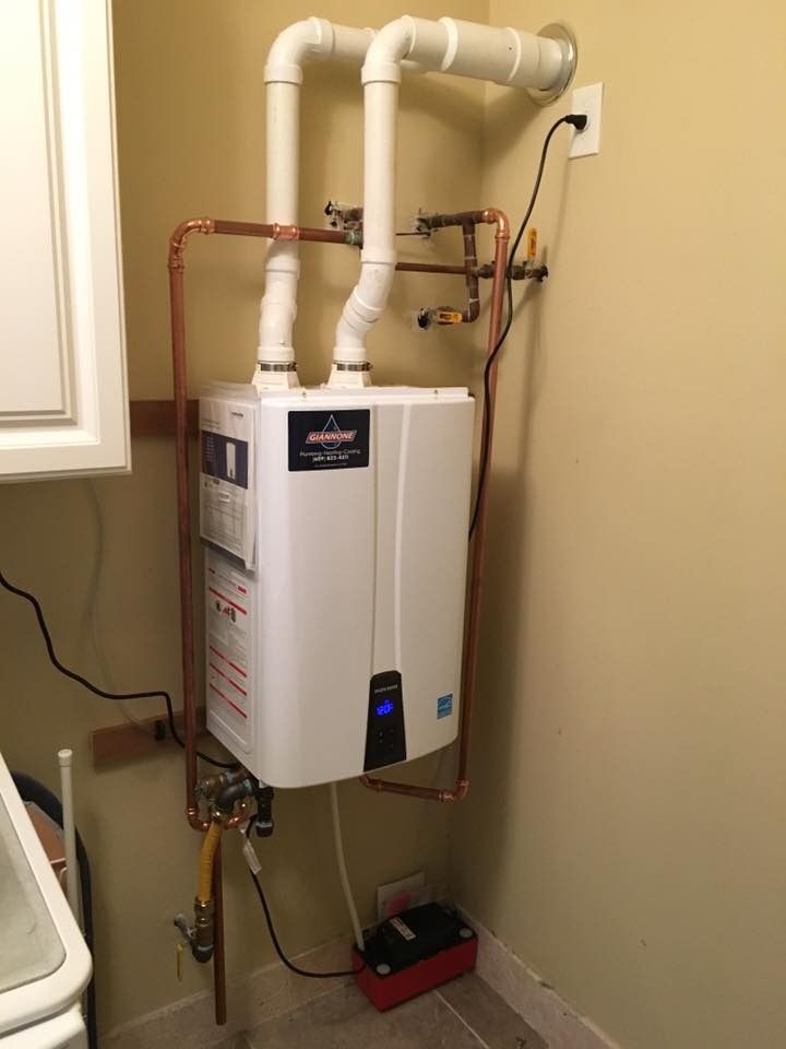 Wall-mounted white water heater with white PVC pipes and a red pump in a utility corner.