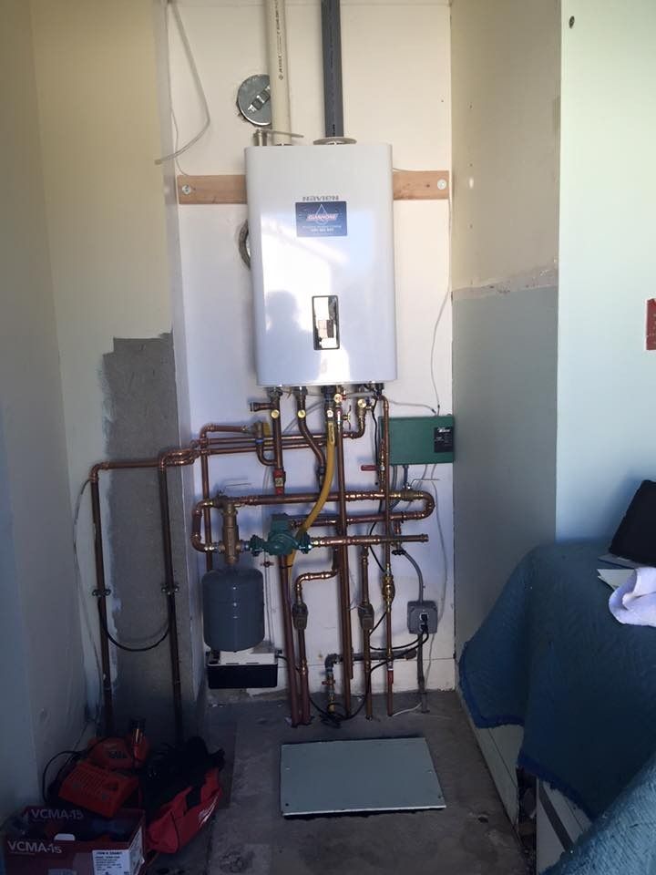 Boiler and exposed copper pipes mounted on a wall in a small utility room