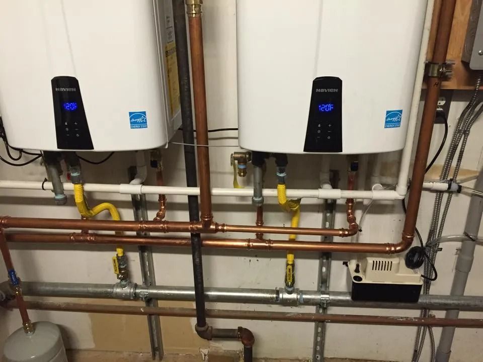 Two white wall-mounted water heaters with copper and yellow piping in a utility room
