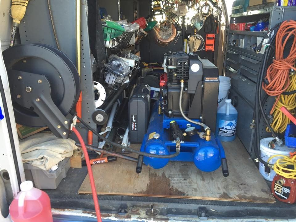 A cluttered garage with a blue air compressor, hoses, tools, and storage items packed along the walls.
