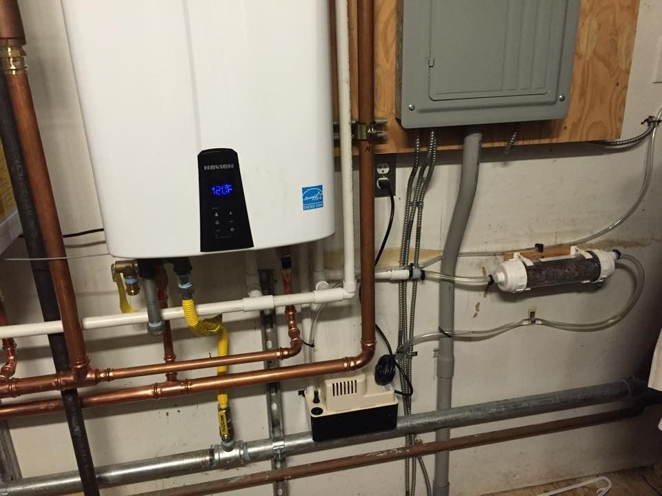 Utility room with wall-mounted boiler, copper pipes, valves, and gray electrical panel on plywood wall