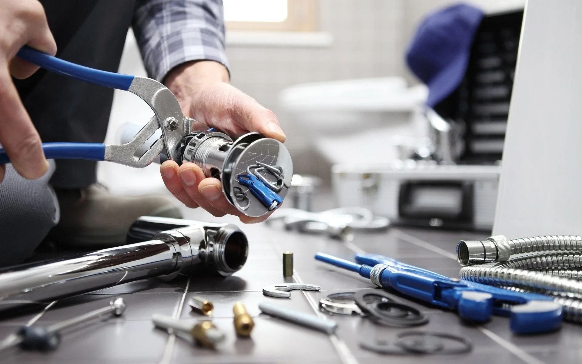Hands using pliers to repair a metal tool on a workbench with scattered hardware