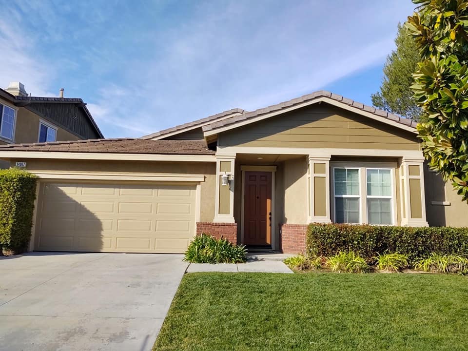 Single-story house with beige exterior, brown door, green lawn, and blue sky.