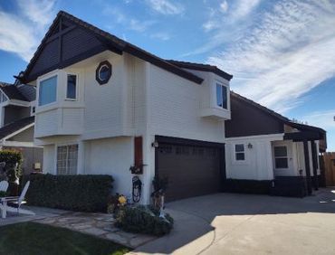 Two-story house with white siding, brown trim, and a dark garage door on a sunny day