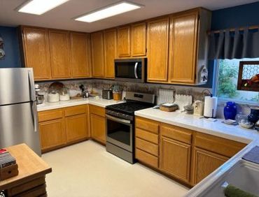 L-shaped kitchen with light wood cabinets, stainless steel appliances, white countertops, and off-white floor