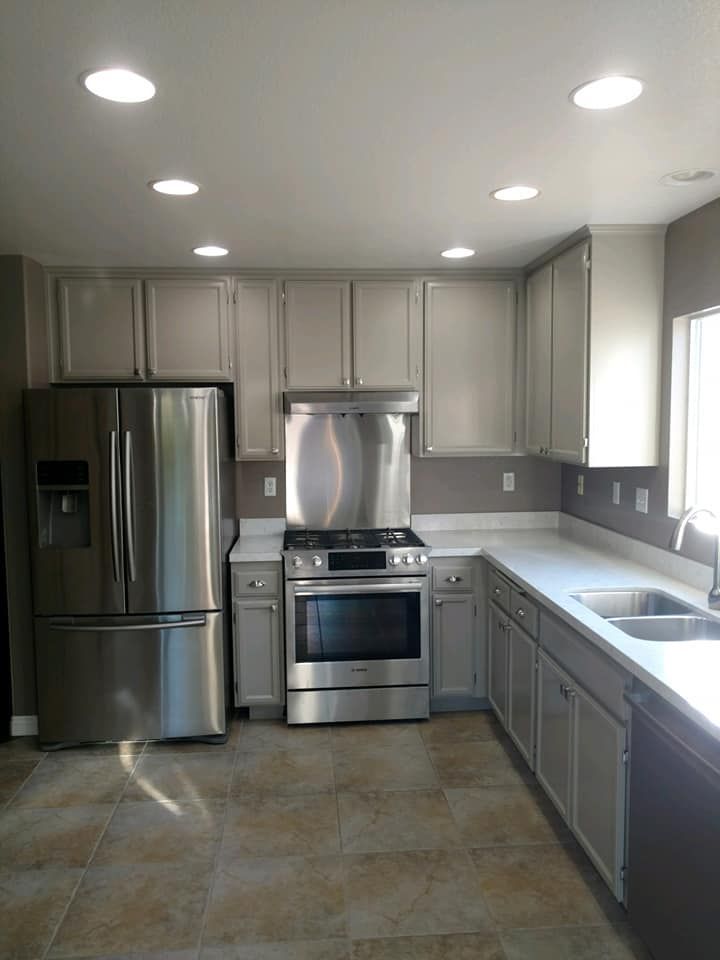 A modern kitchen with stainless steel appliances, gray cabinets, and white countertops.