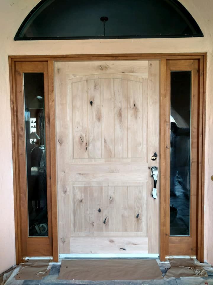Wooden front door with sidelights, arched transom. Light wood, dark trim.