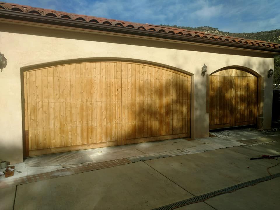 Two arched wooden garage doors in a beige stucco building.