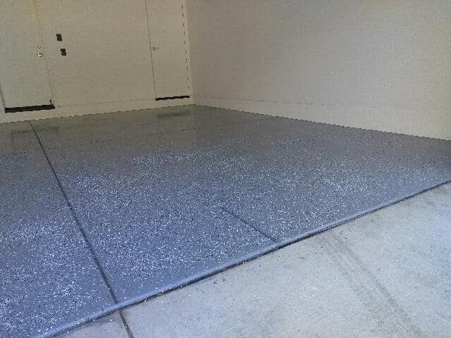 Gray epoxy-coated garage floor. Reflective surface in a mostly empty white-walled garage.